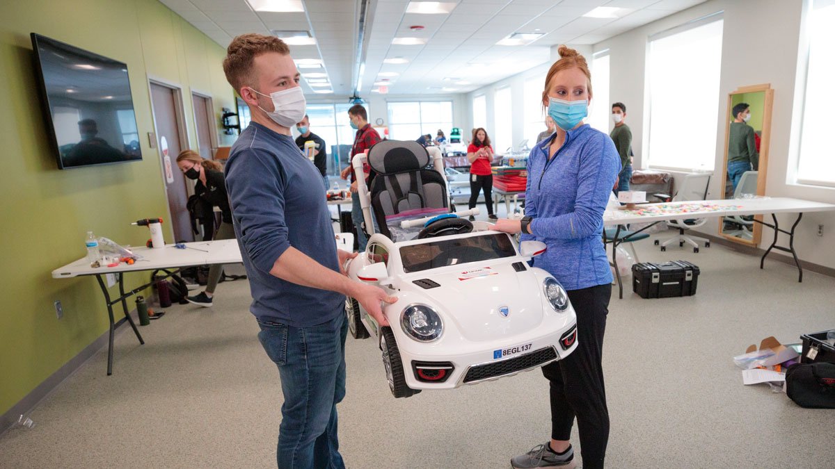 Two students carry an adapted car for a young child 