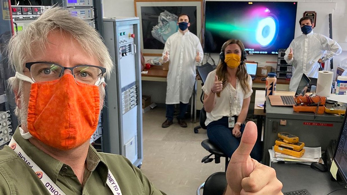 People giving the thumbs-up to the camera at a aerospace company