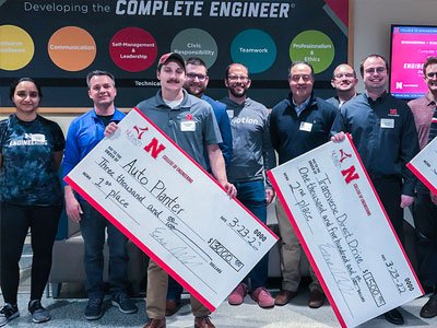 Students holding up large checks they were awarded for winning a competition.